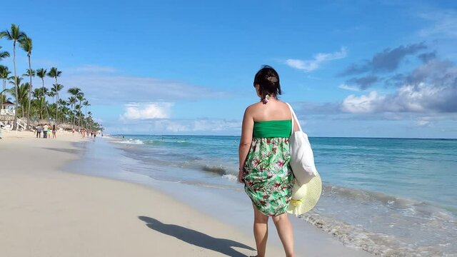 Woman walking on a tropical beach, view to palm trees, sea and white sand. Holidays on paradise nature
