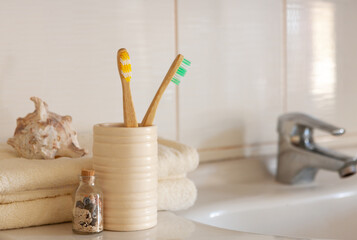 Fototapeta na wymiar Cockleshell, Bath white cotton towels and bamboo toothbrushes on Blurred bathroom interior background with sink and faucet