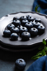 Juicy and ripe blueberries on a gray plate on a dark blue background with a napkin. Close up and macro view