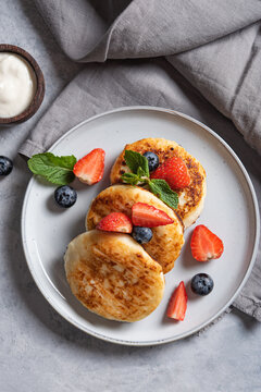 Traditional Russian dish for breakfast  syrniki. Cottage cheese pancakes with sour cream and fresh berries on a blue background with a napkin. Top view image. Vertical orientation