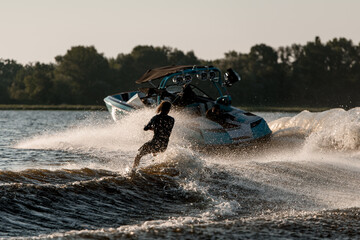 Bright motor boat pulls an active guy riding a wakeboard