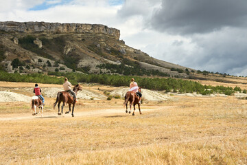  A group of three people rides horses on the prairie along the Rocky Mountains. Selective focus. Copy space.