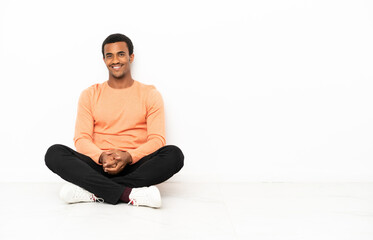 African American man sitting on the floor over isolated copyspace background posing with arms at hip and smiling