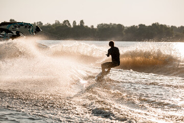 Great view of active man riding wakeboard behind motor boat on splashing river waves. Active and...