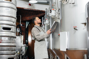 A young bearded brewer monitors the sensor readings during the brewing process. Making beer.