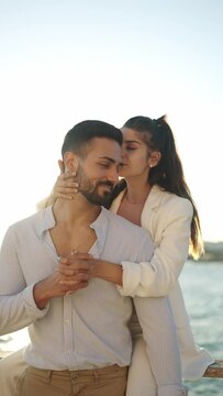 Hispanic woman kissing boyfriend on embankment in sunshine