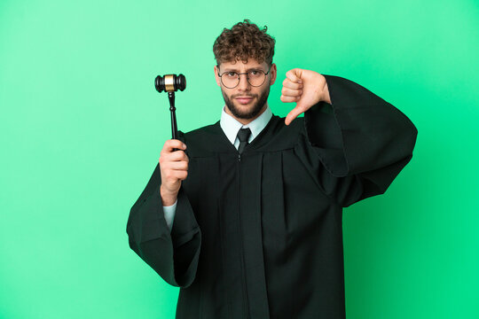 Judge over isolated green background showing thumb down with negative expression
