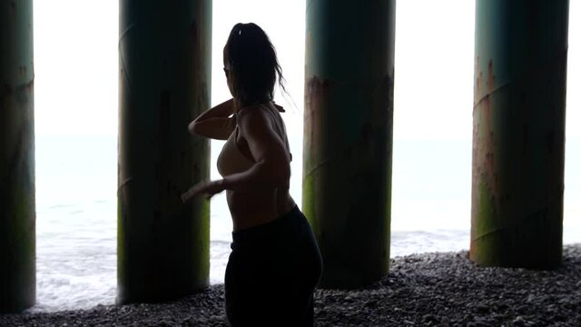 Female Silhouette Against The Background Of Dark Pillars. A Woman Is Dancing. The Average Plan. The Camera Is Moving