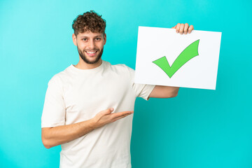 Young handsome caucasian man isolated on blue background holding a placard with text Green check...