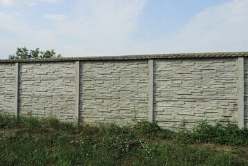 part of a long gray white concrete fence wall on a rural street in green grass