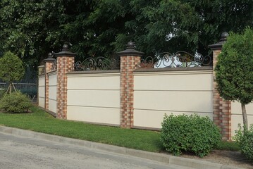 private wall of a fence made of gray concrete and brown bricks outside in green grass