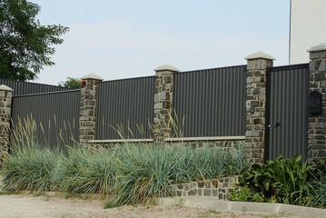 one closed gray metal door and a long wall of iron and stone fence outside in green grass