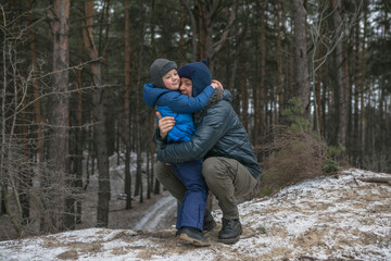 Fototapeta na wymiar Happy family on a walk outdoors in sunny winter forest, Christmas holidays, father and son play together