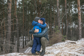 Happy family on a walk outdoors in sunny winter forest, Christmas holidays, father and son play together