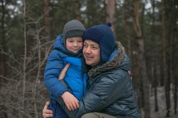 Happy family on a walk outdoors in sunny winter forest, Christmas holidays, father and son play together