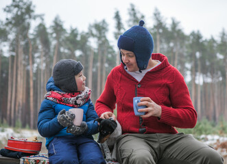 Christmas holidays, father and son drinking  hot New Year beverage. Happy family on a walk outdoors in sunny winter forest