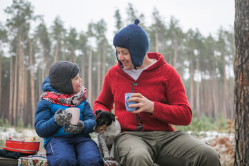 Christmas holidays, father and son drinking  hot New Year beverage. Happy family on a walk outdoors in sunny winter forest