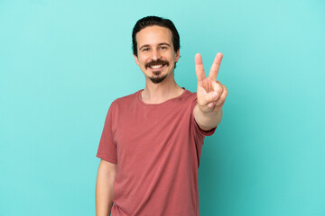 Fototapeta premium Young caucasian man isolated on blue background smiling and showing victory sign