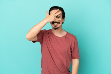 Young caucasian man isolated on blue background covering eyes by hands and smiling