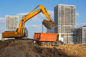 Photo of an excavator and a truck at the construction site of multi-storey buildings in the city