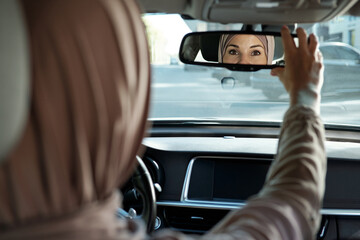 Reflection of face part of Muslim female looking at you in mirror while sitting inside her car