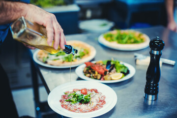 Chef finishing meals in restaurant kitchen pouring olive oil on them