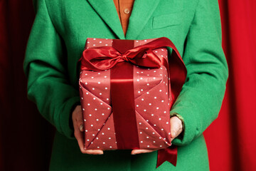 Woman in green jacket with holiday gift box on red curtains background