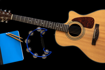 Acoustic guitar, notepad, tambourine on a black background.