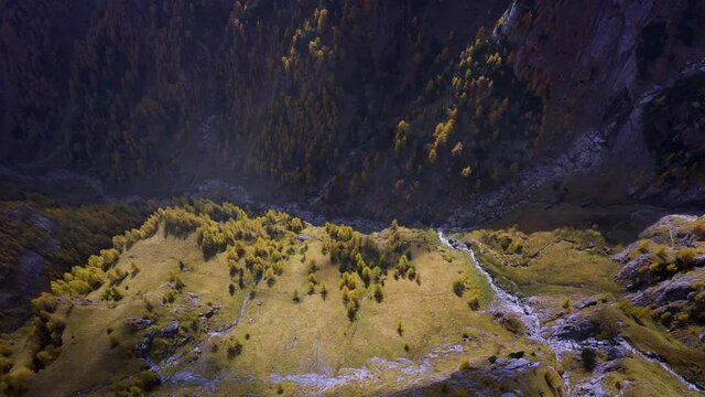 Aerial view of a mountain valley in autumn season. Mountain ridge. Top Down view of a sunny mountain in fall. Areal drone top down throw the clouds. Beautiful autumn colors in the forest.