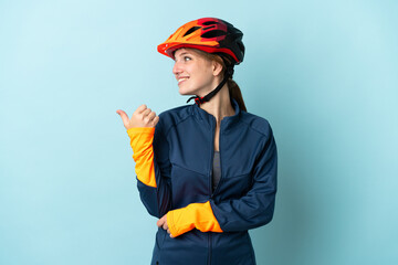 Young cyclist woman isolated on blue background pointing to the side to present a product