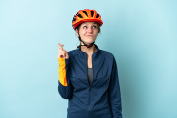 Young cyclist woman isolated on blue background with fingers crossing and wishing the best
