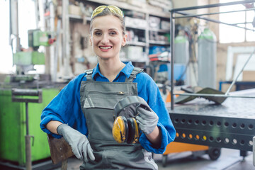 Woman worker in metal factory showing protective workwear, goggles, and ear protection