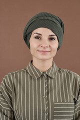 Happy young Muslim businesswoman in headwrap and casualwear looking at you over brown background
