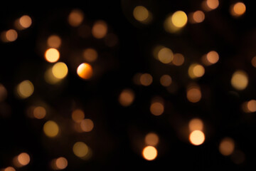 Defocused bokeh lights on black background, an abstract naturally blurred backdrop for Christmas eve or birthday party. Festive light texture. Yellow and red garland in blur. Overlay effect for design