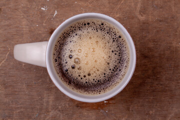 Taza de café solo americano negro en una taza redonda y blanca sobre un fondo marrón de una mesa de madera.