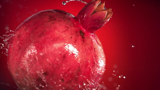 Super slow motion water drips on rotating pomegranate . On a black background.