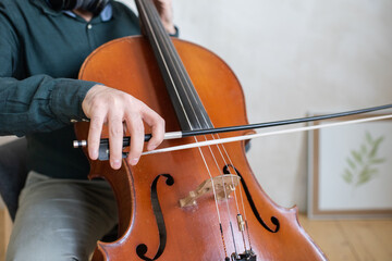 Hand of young cello player gliding fiddlestick across strings while performing piece of music in front of camera