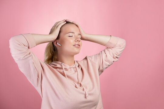 Dancing with her music, a young woman in a pink hoodie dances with wireless headphones in her ears. Enjoy a personalized playlist
