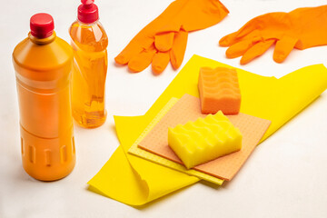 Bottle of orange liquid, yellow sponge, and yellow rag. Rubber orange gloves.
