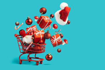 Christmas composition with shopping cart with flying gifts, ornaments, candy canes and Santa cap on vibrant blue background. Creative Xmas or New year concept. Festive shopping or advertisement idea.