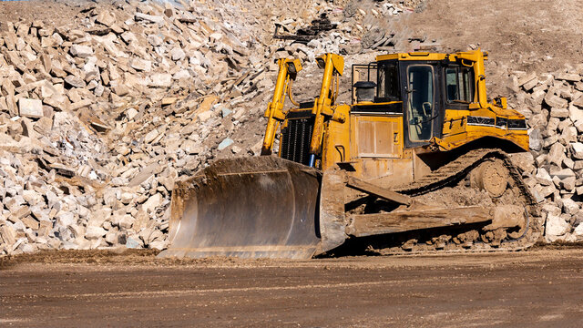 Yellow bulldozer working in front of a large pile of rock, gravel, and dirt