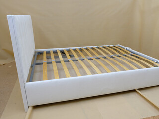 Production. Bed upholstered in white fabric without mattress. Wooden slats. 