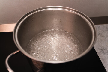 Boiling water in a metal saucepan on the black surface of an induction cooker