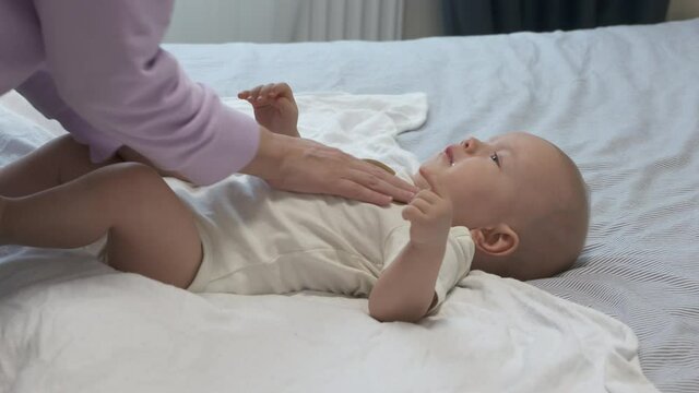 Mother swaddling baby before bedtime, 7 month old infant wrapped on bed, swaddling helps prevent baby from flailing arms and legs. High quality 4k footage