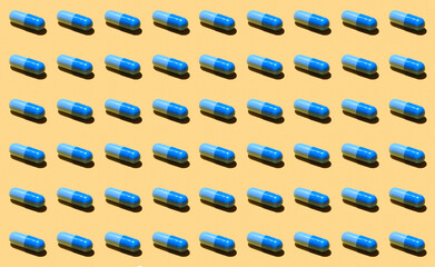 Pills pattern. Set of blue tablets isolated on yellow background. Pattern made with pharmaceutical medicine capsules on yellow background. Medicine concept.