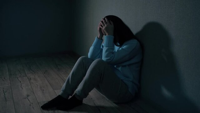 Upset woman in blue sweater and pants sits leaning on wall on parquet floor in freshly renovated room feeling depressed by quarrel over reconstruction.