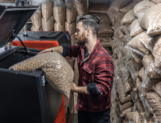 The man loads the pellets in the solid fuel boiler, working with biofuels.