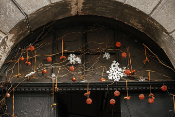 Stylish simple christmas decoration with branches and orange ornaments on window or door. Christmas festive street decor for winter holidays in european city street. Merry Christmas!