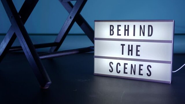 Behind the scene light box. Black text on white lightbox of word Behind the scenes. prop include megaphone movie clapperboard and director chair in studio. footage for video production making of.