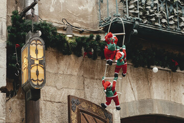 Stylish little santa clauses climbing on ladder on balcony of old building, christmas decoration outdoor. Christmas festive decor for winter holidays in european city street. Merry Christmas!